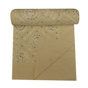 Puede incluir: Una tela beige con bordados blancos y pequeños detalles de espejo. La tela está enrollada y doblada por la mitad.