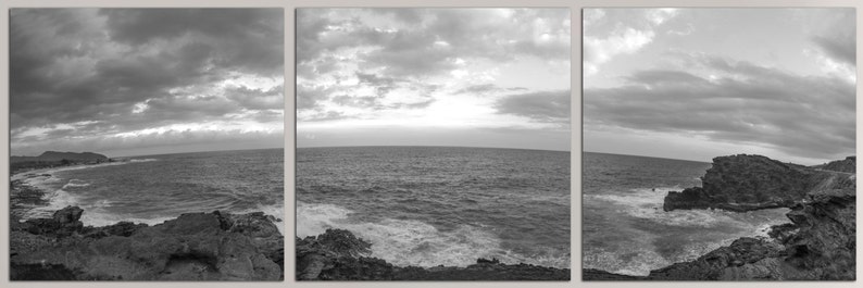 May include: A black and white panoramic photograph of a rocky coastline with crashing waves and a cloudy sky.