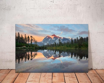 May include: A landscape canvas print featuring a mountain range reflected in a calm lake. The sky displays a gradient of colors, from orange and pink to blue, with clouds. The foreground shows the lake and the reflection of the mountains and trees.