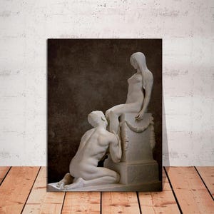 May include: A black and white photograph of two statues. The statues are of a man and a woman. The woman is sitting on a pedestal and the man is kneeling at her feet. The statues are in a dark room.