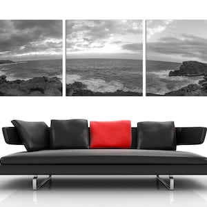 May include: A black leather sofa with three pillows, one red pillow in the center, and two black pillows on either side. The sofa is in front of a wall with three black and white photographs of a seascape.