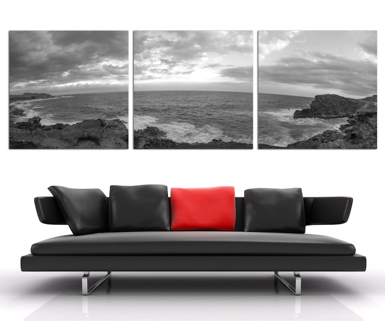 May include: A black leather sofa with three pillows, one red pillow in the center, and two black pillows on either side. The sofa is in front of a wall with three black and white photographs of a seascape.
