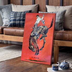 May include: A canvas print featuring a vintage illustration of a rodeo cowboy on a bucking bronco against a red background. The artwork includes the text "LET 'ER BUCK" in the lower left corner. The cowboy is wearing a white shirt and hat.
