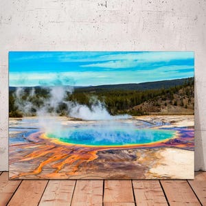 May include: A vibrant aerial view of a natural hot spring in Yellowstone National Park. The spring is a circular pool of turquoise blue water surrounded by a ring of orange, yellow, and red. Steam rises from the water, creating a hazy atmosphere.