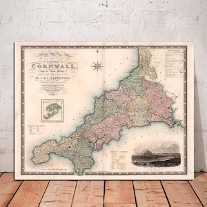 May include: An antique map of Cornwall, England, printed in black, brown, green, pink, and blue ink on cream paper. The map shows the county's boundaries, towns, and rivers. The title "The County of Cornwall" is printed at the top of the map.