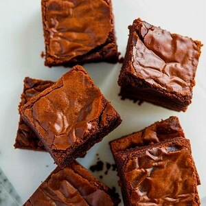 Pu&ograve; includere: Vista dall'alto di sei brownies quadrati con un ricco colore marrone scuro. I brownies hanno una superficie leggermente screpolata e strutturata, che suggerisce un interno morbido. Disposti su una superficie bianca.