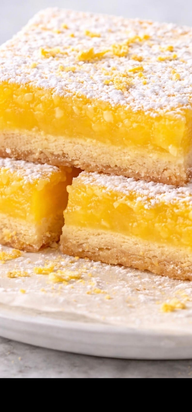 May include: Close-up of lemon bars dusted with powdered sugar. The bars have a buttery, golden crust and a bright yellow, citrusy filling. The dessert is arranged on a white plate.