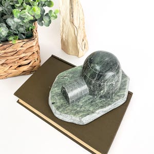 May include: A green stone sculpture of an igloo with a small entrance. The sculpture is sitting on a brown book.