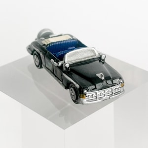 May include: A black toy car with a white roof and chrome accents. The car is a convertible with a blue interior and a spare tyre on the back.