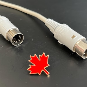 Könnte beinhalten: Zwei graue DIN-Stecker mit einem roten Ahornblatt-Pin in der Mitte. Die Stecker haben eine silberne Metallspitze mit fünf Stiften.