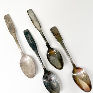 May include: Four silver spoons with different engraved designs. The spoons have a traditional shape with a rounded bowl and a long handle.