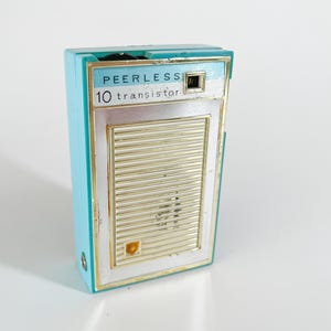 May include: A vintage blue and silver Peerless 10 transistor radio. The radio has a gold grille and a small window on the top.