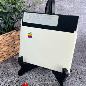 May include: A white Apple II floppy disk with a black label that reads "EDUCATIONAL TECHNOLOGY PROGRAM Cat. No. 29539 (Diskette) ETP Apple 86 01 Sequencing". The disk is in a white plastic case with a black stand.