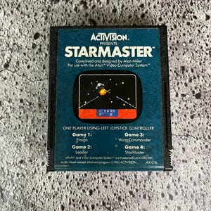 May include: A blue Atari video game cartridge for StarMaster, a game conceived and designed by Alan Miller. The cartridge is for use with the Atari Video Computer System. The text "E: 9698" and "0: W" are visible on the cartridge.