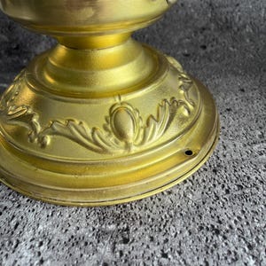 Peut inclure: Gros plan d'un plafonnier vintage en laiton. Le luminaire présente une base décorative avec des motifs floraux en relief et un abat-jour en verre dépoli. Le laiton a une patine chaude et vieillie.