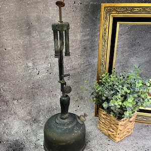 Puede incluir: Una lámpara de queroseno antigua de metal negro con un brazo largo y ajustable y una base redonda. La lámpara tiene un mango de madera y una perilla de metal para ajustar la llama.