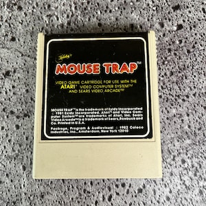 May include: A black and white Atari video game cartridge for the Atari Video Computer System. The cartridge is labeled "MOUSE TRAP" and includes copyright information for Exidy Incorporated, Atari, and Sears, Roebuck and Co. The cartridge is printed in the USA.
