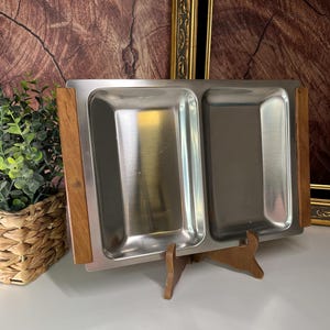 Puede incluir: Una bandeja de servir de acero inoxidable con dos compartimentos, con un marco y un soporte de madera. La bandeja es ideal para servir aperitivos, aperitivos o condimentos.