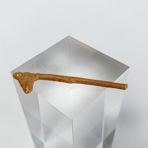 Puede incluir: Un hacha de guerra de madera marrón con una cabeza tallada, expuesta sobre un pedestal de vidrio transparente.