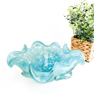 Può includere: Una ciotola di vetro blu chiaro con un design bianco macchiato. La ciotola ha una forma ondulata e organica ed è perfetta per contenere oggetti decorativi o servire spuntini.