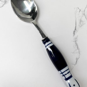Puede incluir: Una cuchara de plata con un mango de porcelana azul y blanco. El mango tiene un patrón geométrico.