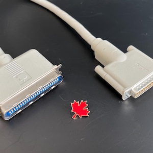 Könnte beinhalten: Zwei graue Computerkabel mit unterschiedlichen Steckern. Ein Kabel hat einen 25-poligen Stecker und das andere einen 9-poligen Stecker.