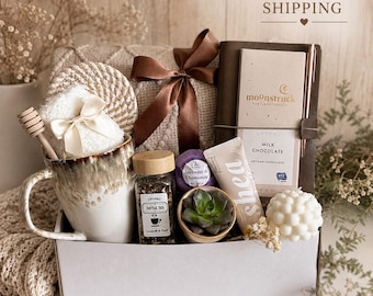 May include: A gift box containing a ceramic mug with a honey dipper, a jar of herbal tea, a lavender and chamomile bath bomb, a succulent in a small pot, a tube of shea cream, a white bubble candle, a chocolate bar, a pen, and a notebook.