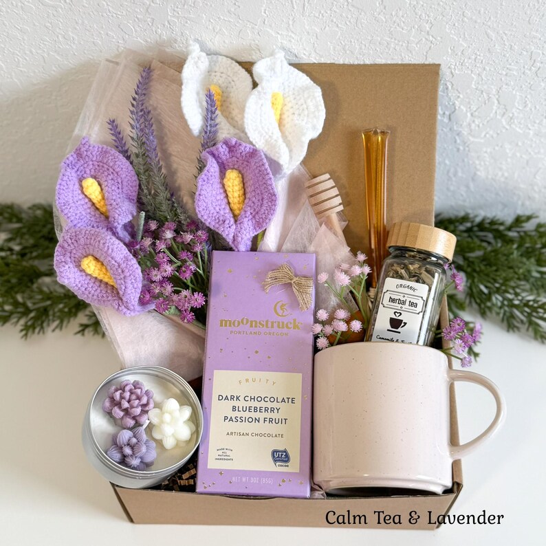 May include: A gift box containing a light pink ceramic mug, a Moonstruck dark chocolate bar with blueberry and passion fruit, a jar of organic herbal tea, a wooden honey dipper, and a tin with three small succulent-shaped candles.