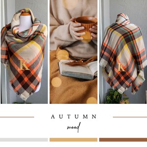 May include: A plaid blanket scarf featuring a pattern of cream, brown, orange, and yellow stripes with a gold embroidered letter K on the front. The scarf has a frayed edge finish and is displayed on a mannequin in a triangular folded style.