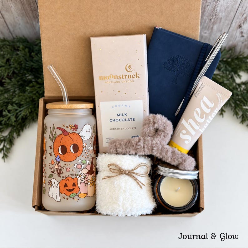Pu&ograve; includere: Una confezione regalo contenente un bicchiere in vetro satinato con stampa di zucche, una tavoletta di cioccolato al latte Moonstruck, un diario blu navy con penna, un fermaglio per capelli peloso, un oggetto in peluche e una candela.