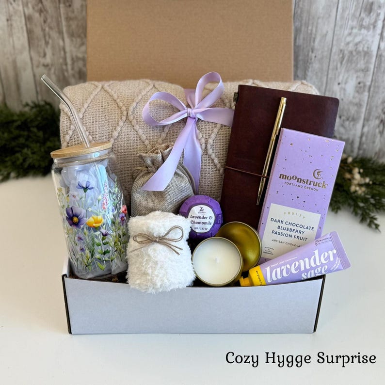 Pu&ograve; includere: Una confezione regalo contenente un bicchiere di vetro con stampa floreale e cannuccia, una coperta in maglia beige con nastro color lavanda, un diario marrone scuro con penna dorata, una tavoletta di cioccolato Moonstruck, un tubetto lavanda salvia, una candela e un sacchetto.