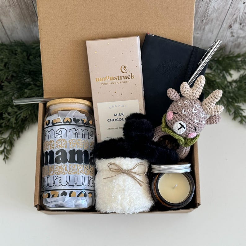 K&ouml;nnte beinhalten: Eine Geschenkbox mit einem Glastrinkbecher mit Bambusdeckel und dem Wort mama in Schwarz, einer Moonstruck-Milchschokolade, einem schwarzen Notizbuch mit silbernem Stift, einem geh&auml;kelten Rentier, flauschigen wei&szlig;en Socken und einer kleinen Kerze.