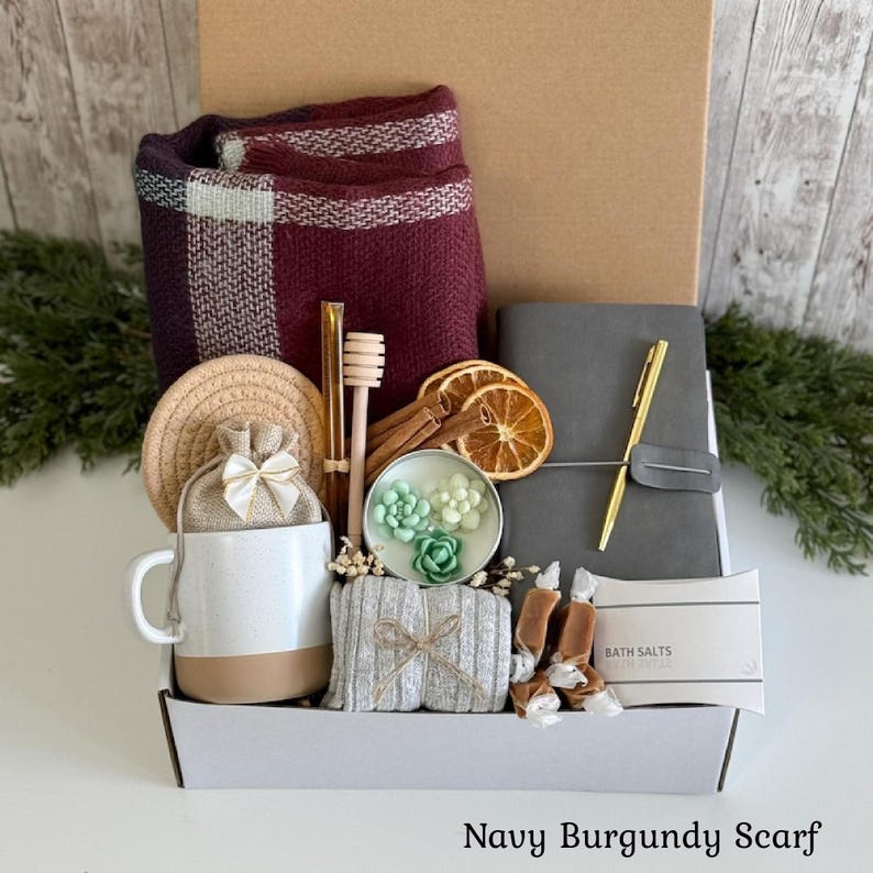Pu&ograve; includere: Una confezione regalo contenente una sciarpa a quadri bordeaux, una tazza in ceramica bianca e beige, un piccolo sacchetto beige con coulisse e fiocco bianco, un taccuino grigio con penna dorata, un bastoncino per miele, arance essiccate e sali da bagno.