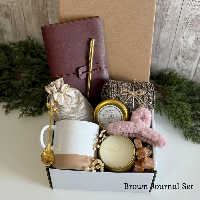 Pu&ograve; includere: Una scatola regalo contenente un diario marrone scuro con una penna dorata, una tazza in ceramica bianca e beige, un cucchiaio dorato, un sacchetto in tela beige, una candela profumata in barattolo dorato, un capo in maglia marrone, una molletta rosa e dolci.