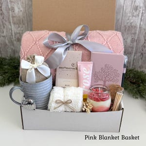 Pu&ograve; includere: Una confezione regalo contenente una coperta in maglia rosa con un nastro grigio, una tazza grigia con un infusore per t&egrave; a forma di cuore, una barretta di cioccolato al latte Moonstruck, una crema mani alla rosa, un diario rosa e una candela.