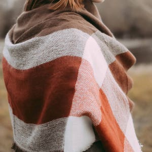 May include: A woman wearing a brown, white, and red plaid scarf. The scarf has a fringe border.