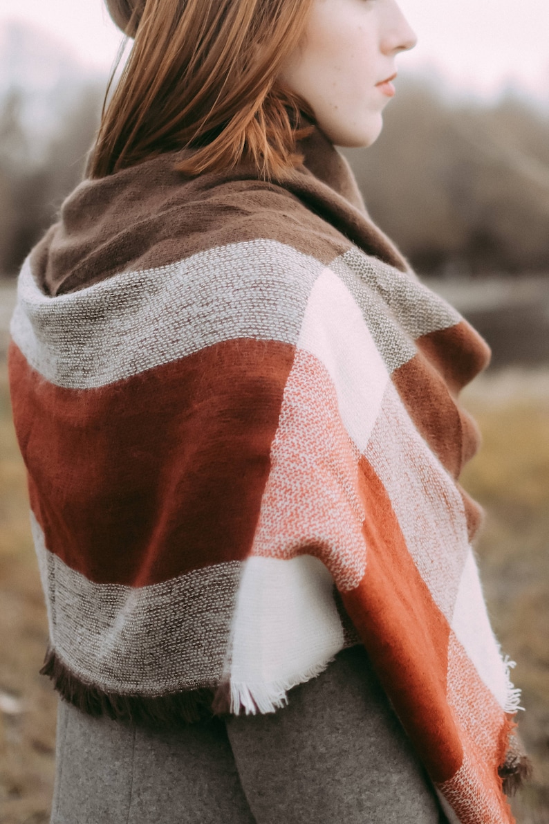 May include: A woman wearing a brown, white, and red plaid scarf. The scarf has a fringe border.