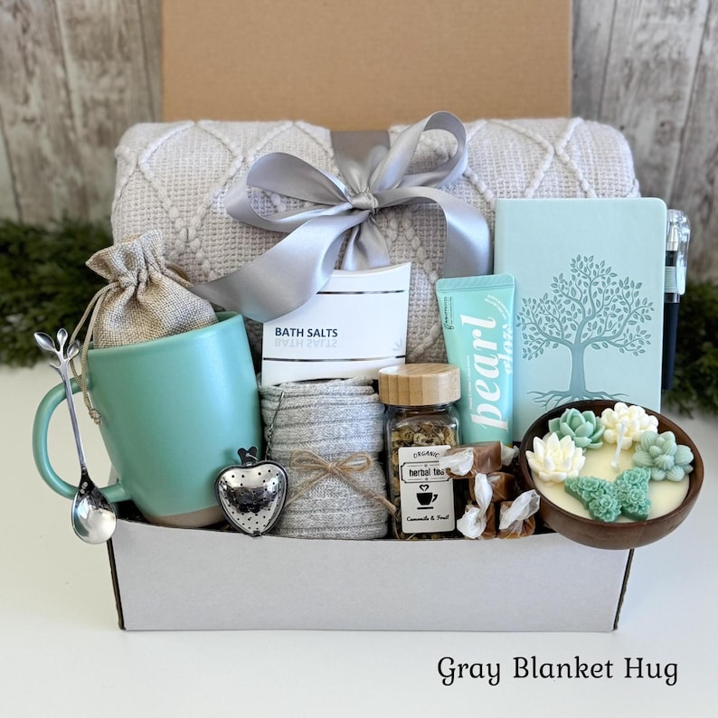 Pu&ograve; includere: Una confezione regalo contenente una coperta grigio chiaro testurizzata con un nastro argentato, una tazza color ottanio, un infusore per t&egrave; argentato a forma di cuore, un sacchetto di juta, un barattolo di tisana, una crema Pearl e una candela.