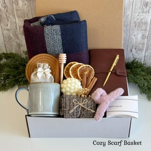Pu&ograve; includere: Una confezione regalo contenente una sciarpa a quadri blu navy e bordeaux, una tazza azzurra a coste, un diario in pelle marrone con penna dorata, una candela a bolle, fette d'arancia essiccate, cannella, un bastoncino per miele e sali da bagno.