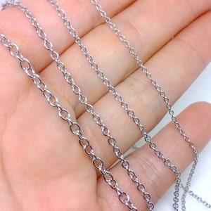 Puede incluir: Cuatro cadenas plateadas de diferentes longitudes, dispuestas sobre una mano.