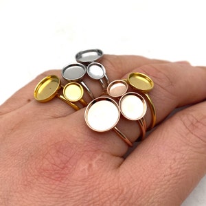 Könnte beinhalten: Ein Satz von fünf Ringen mit runden, gefassten, leeren Metalltabletts. Die Ringe sind in Silber, Gold und Roségold.