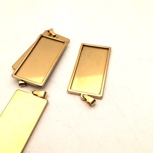 Peut inclure: Trois plateaux de pendentif en métal de couleur dorée de forme rectangulaire avec une boucle en haut pour la suspension. Les plateaux sont vierges et prêts à être personnalisés.