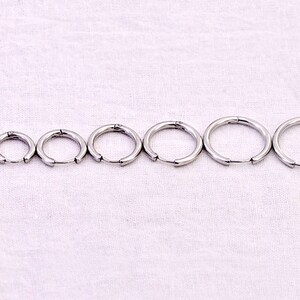 May include: A set of eight silver hoop earrings of varying sizes. The earrings are arranged in order of size, with the smallest earring on the left and the largest earring on the right.