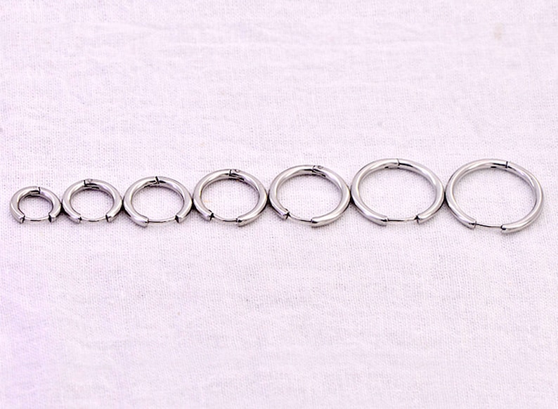May include: A set of eight silver hoop earrings of varying sizes. The earrings are arranged in order of size, with the smallest earring on the left and the largest earring on the right.