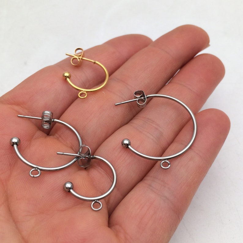May include: Three pairs of hoop earring findings, two silver and one gold. Each earring has a small ball at the top and a jump ring at the bottom.