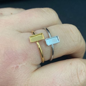 Puede incluir: Dos anillos ajustables con engastes rectangulares. Un anillo es dorado y el otro es plateado.