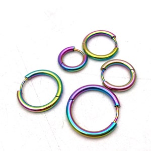 Puede incluir: Cuatro pendientes de aro iridiscentes de diferentes tamaños. Los pendientes son de metal y tienen un acabado arcoíris.