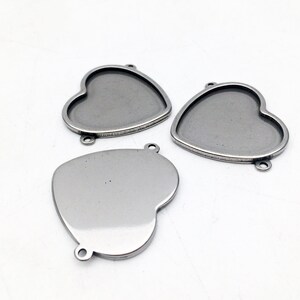 May include: Three silver heart-shaped metal frames with a smooth, shiny finish. The frames have a rounded edge and three holes for attaching to jewelry or other crafts.
