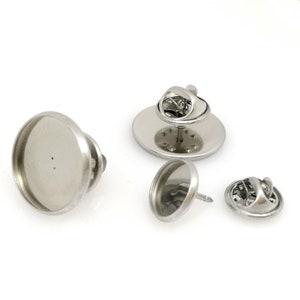 May include: Three silver-toned metal pin back settings for crafting. The settings are round and have a flat surface for attaching a design. The settings are shown from different angles.