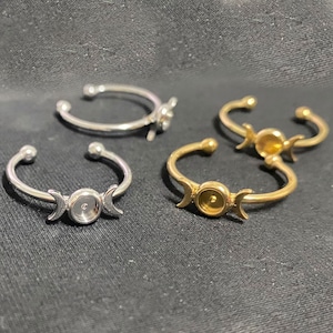 Può includere: Due anelli regolabili in argento e oro con un design a tripla luna. Gli anelli sono aperti sul retro e hanno una lunetta rotonda per aggiungere un ciondolo o una pietra.
